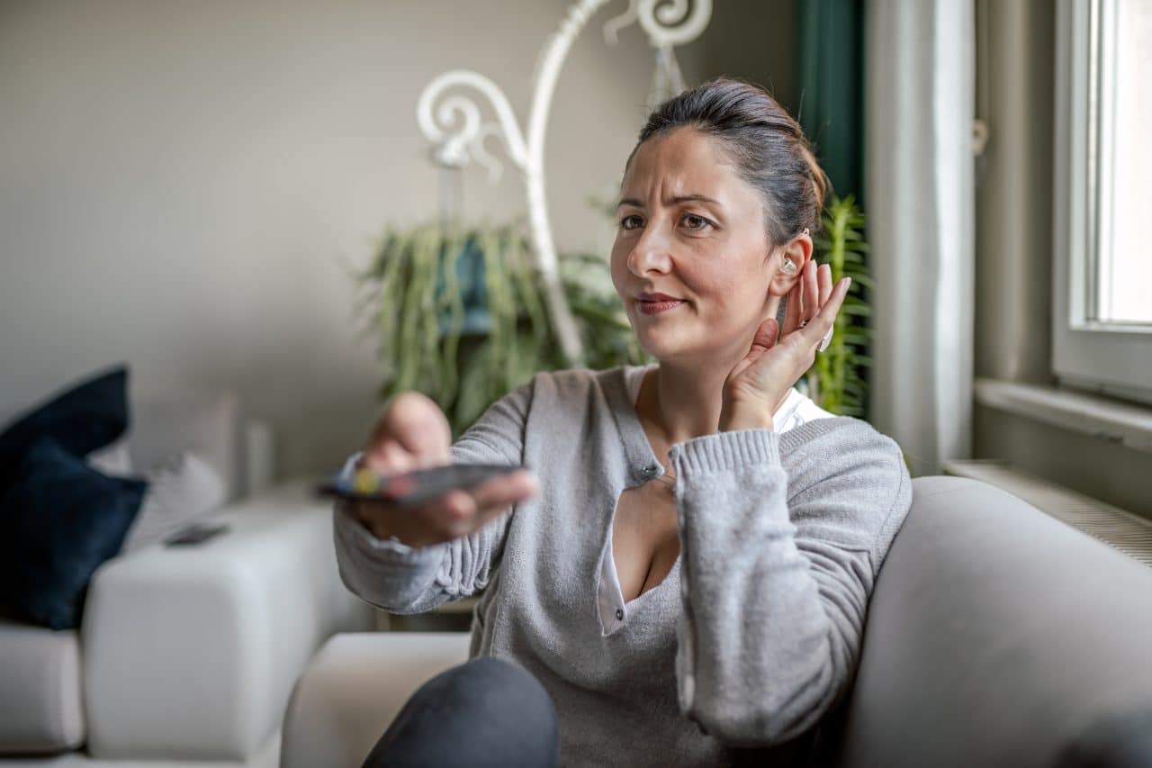 Woman adjusting her hearing aid while watching TV.