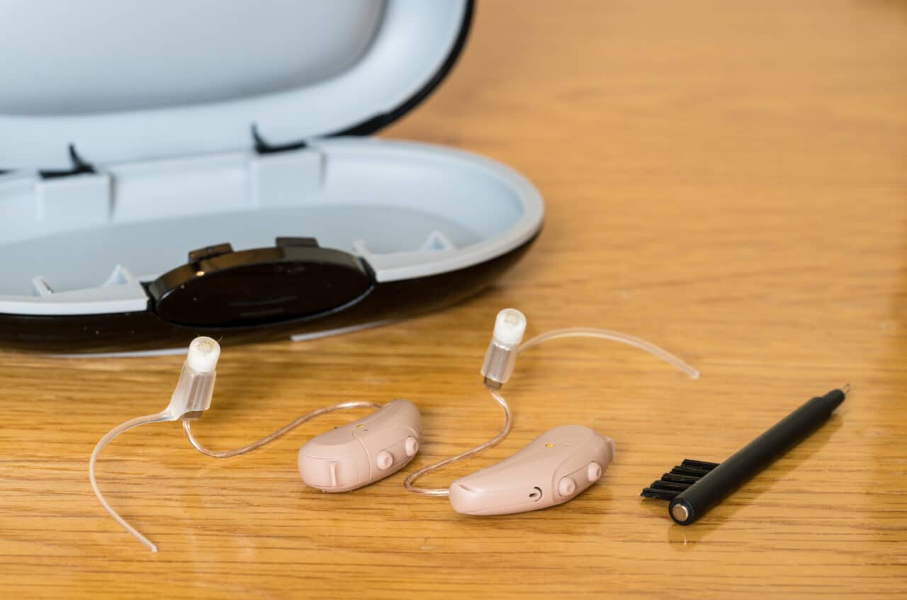 Modern hearing aids with case and brush on wooden bedside dressing table.