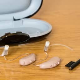 Modern hearing aids with case and brush on wooden bedside dressing table.